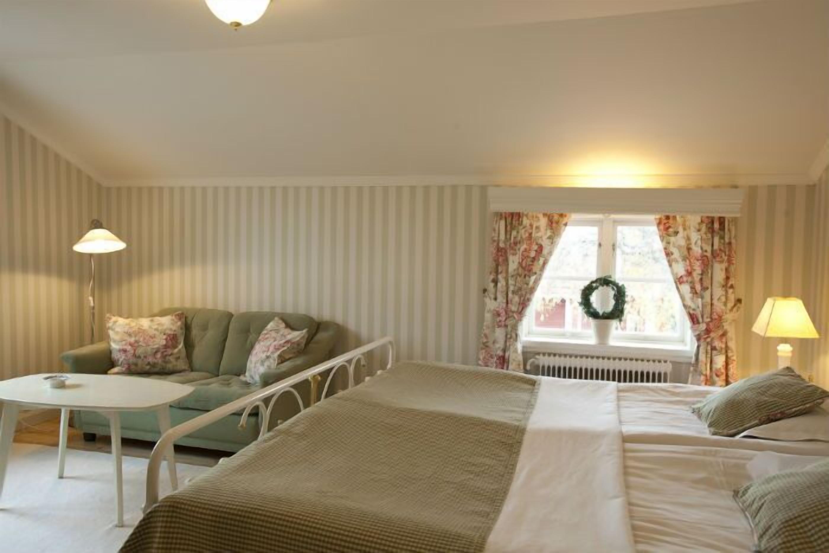 A bedroom with a bed, a sofa, a small table, and a window with curtains.