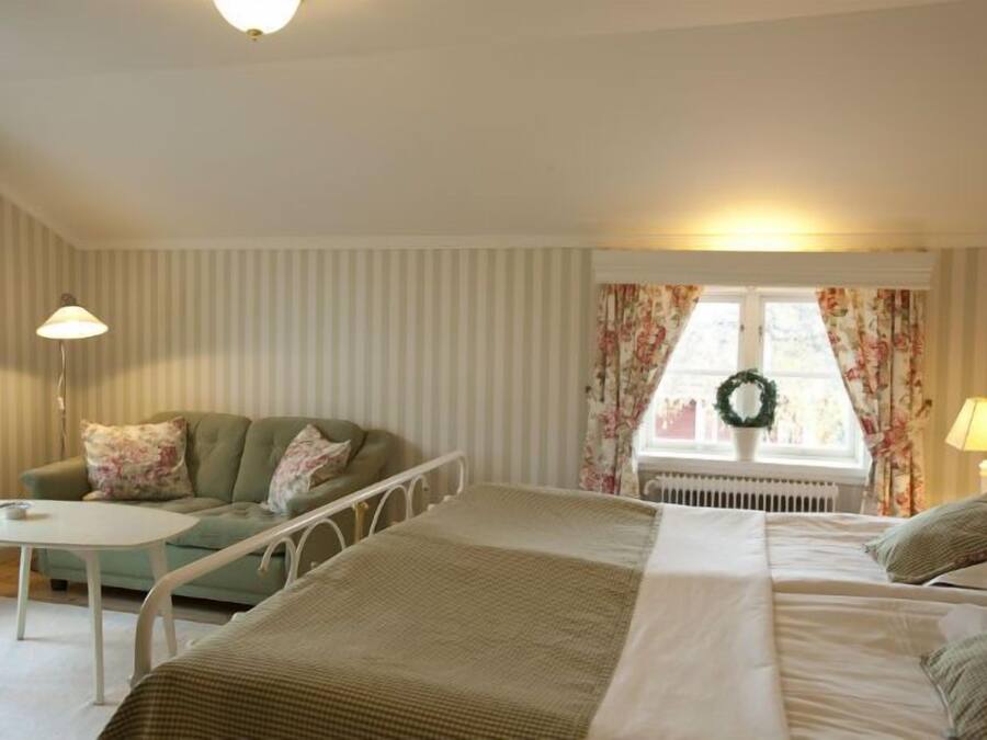 A bedroom with a bed, a sofa, a small table, and a window with curtains.