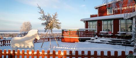 A snow-covered outdoor area with a wooden fence, a white horse sculpture, and a building with a red facade and the name "Calbergsgarden".