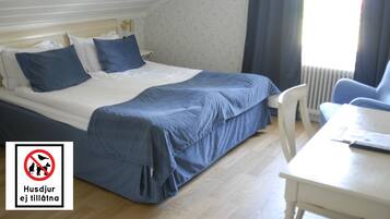 A bedroom with a bed, pillows, a desk, and a chair. There is a window with curtains and a radiator.