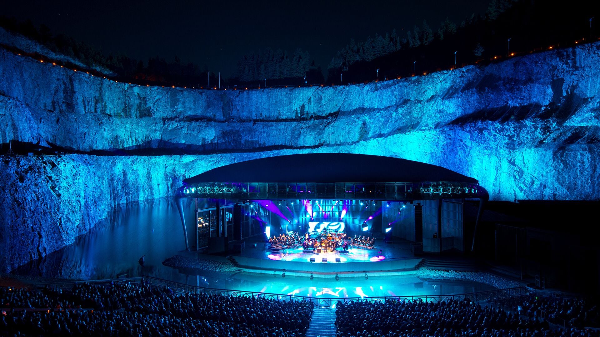 An indoor concert venue with a stage, seating, and a large audience.