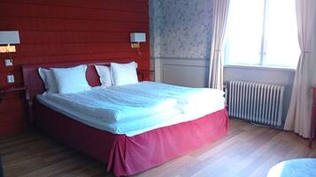 Una cama en una habitación con cabecera roja, un radiador y una ventana con cortinas.