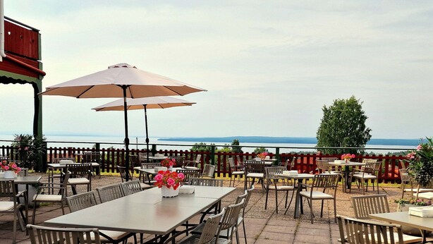 Une terrasse extérieure avec des tables et des chaises, une clôture en bois et une vue sur la mer.