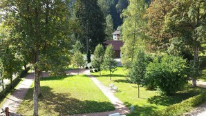 A residential area with a paved pathway, green lawns, and trees. There are white benches along the path and a house in the background. - Hotel Waldeck (Todtmoos)