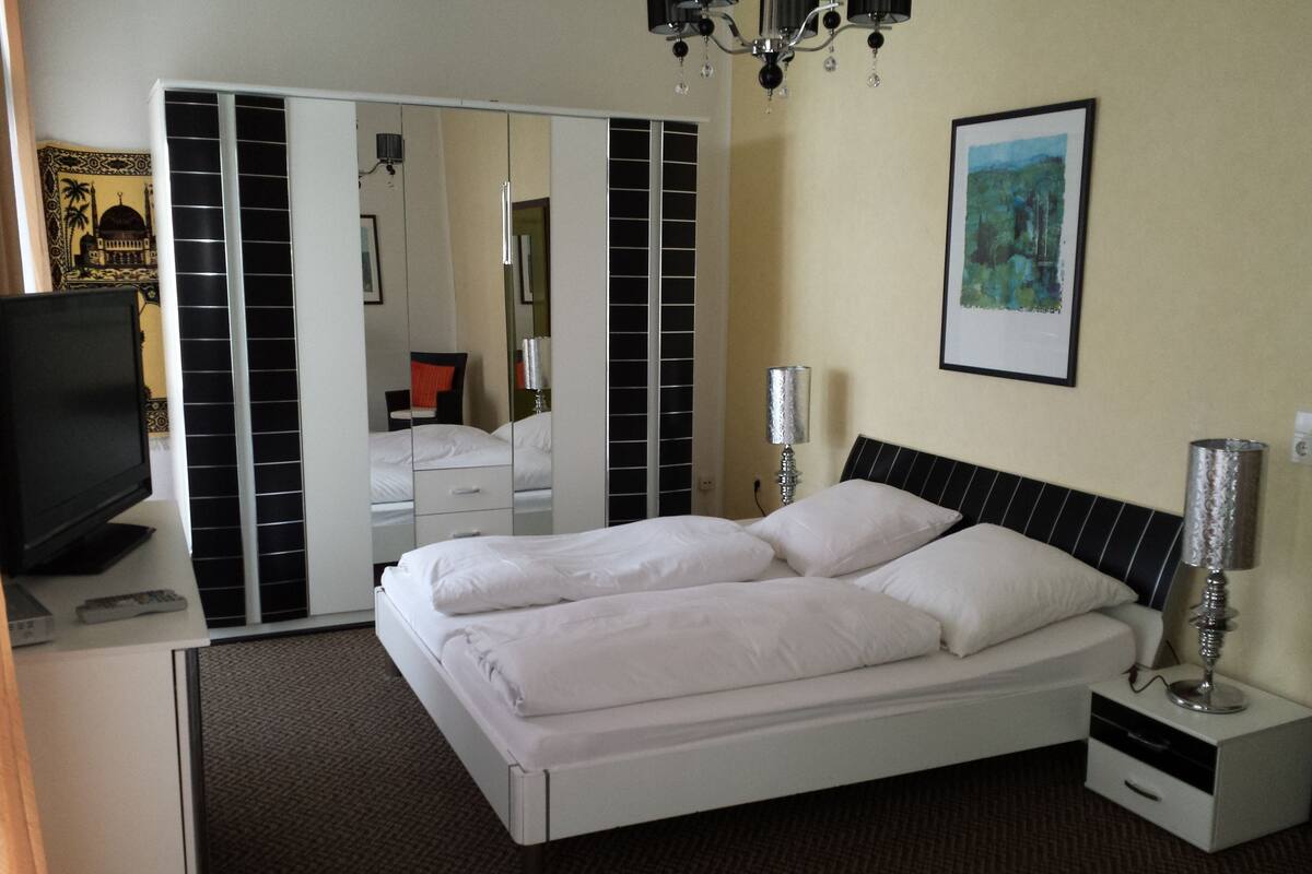 A hotel room with a bed, a TV, a mirror, and a painting on the wall.