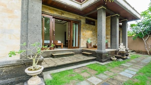 A stone house with a tiled patio, a wooden door, and a small garden with a potted plant. - Pondok Baruna Garden Rooms (Lembongan Island)