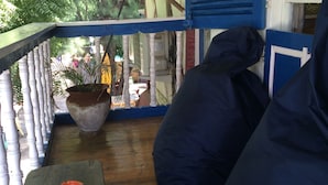 A covered porch with a wooden table and a bench, a potted plant, and a view of the surrounding greenery. - Le Petit Gili (Gili Trawangan)