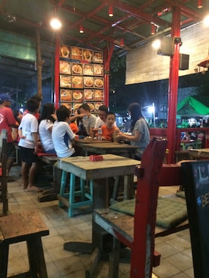 A restaurant with wooden tables and chairs, a high ceiling with exposed beams, and a wall displaying various food items.