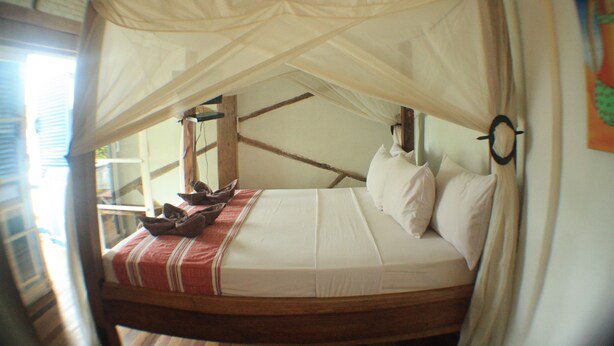 A bed with a canopy, wooden beams, and a red and white striped blanket. - Le Petit Gili (Gili Trawangan)