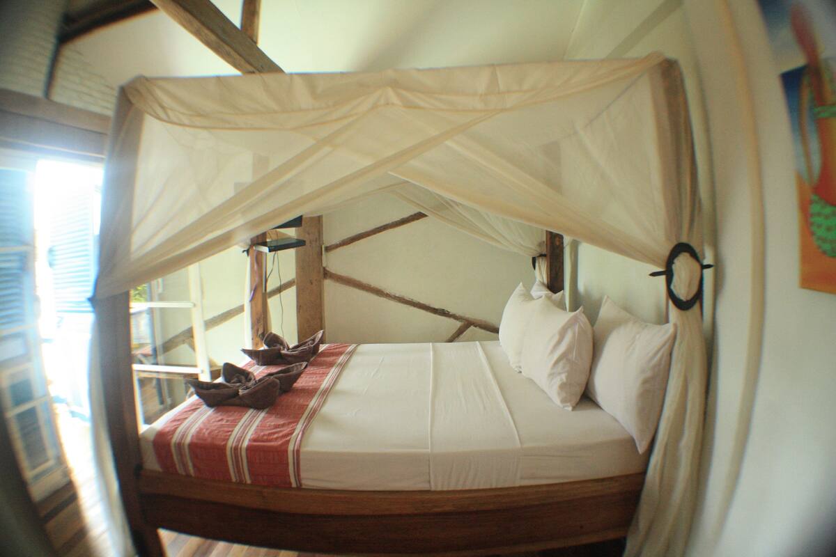 A bed with a canopy, wooden beams, and a red and white striped blanket.