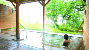 Eine Holzterrasse mit Whirlpool, umgeben von Grünpflanzen und Bäumen.