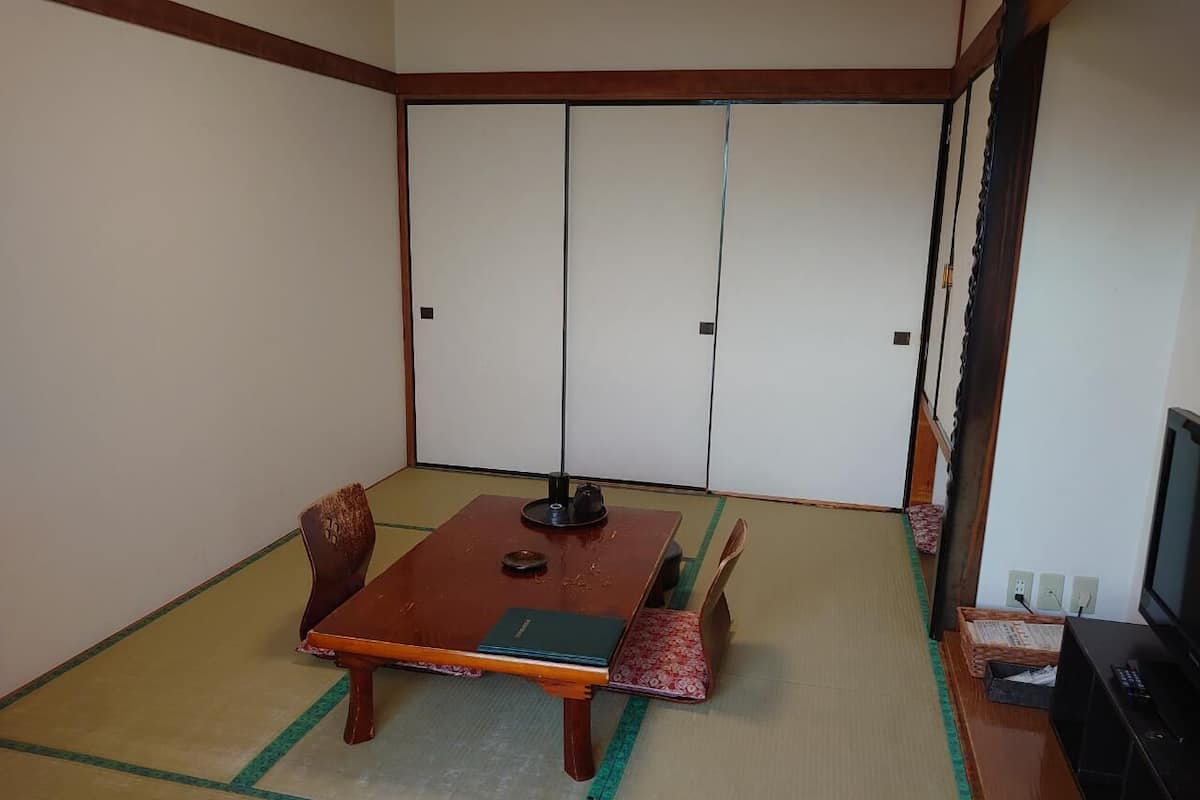 A tatami mat room with a low wooden table, two chairs, a television, and a sliding door.
