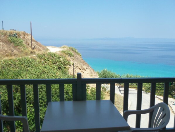 A table and chairs on a balcony overlooking a coastal view with a clear sky.