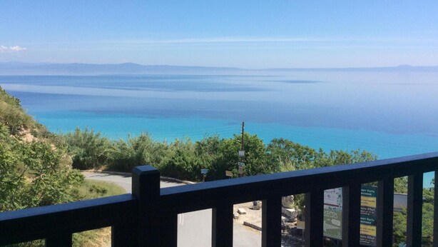 A coastal view from a balcony with a clear sky, a road, and greenery.