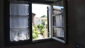 A window with lace curtains, a view of a courtyard with buildings, and a tiled wall.