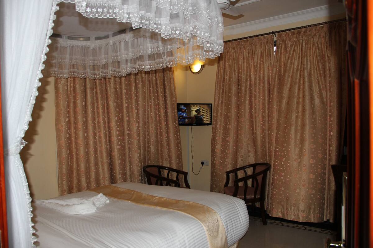 Un dormitorio con cama, dos sillones, televisor y cortinas.