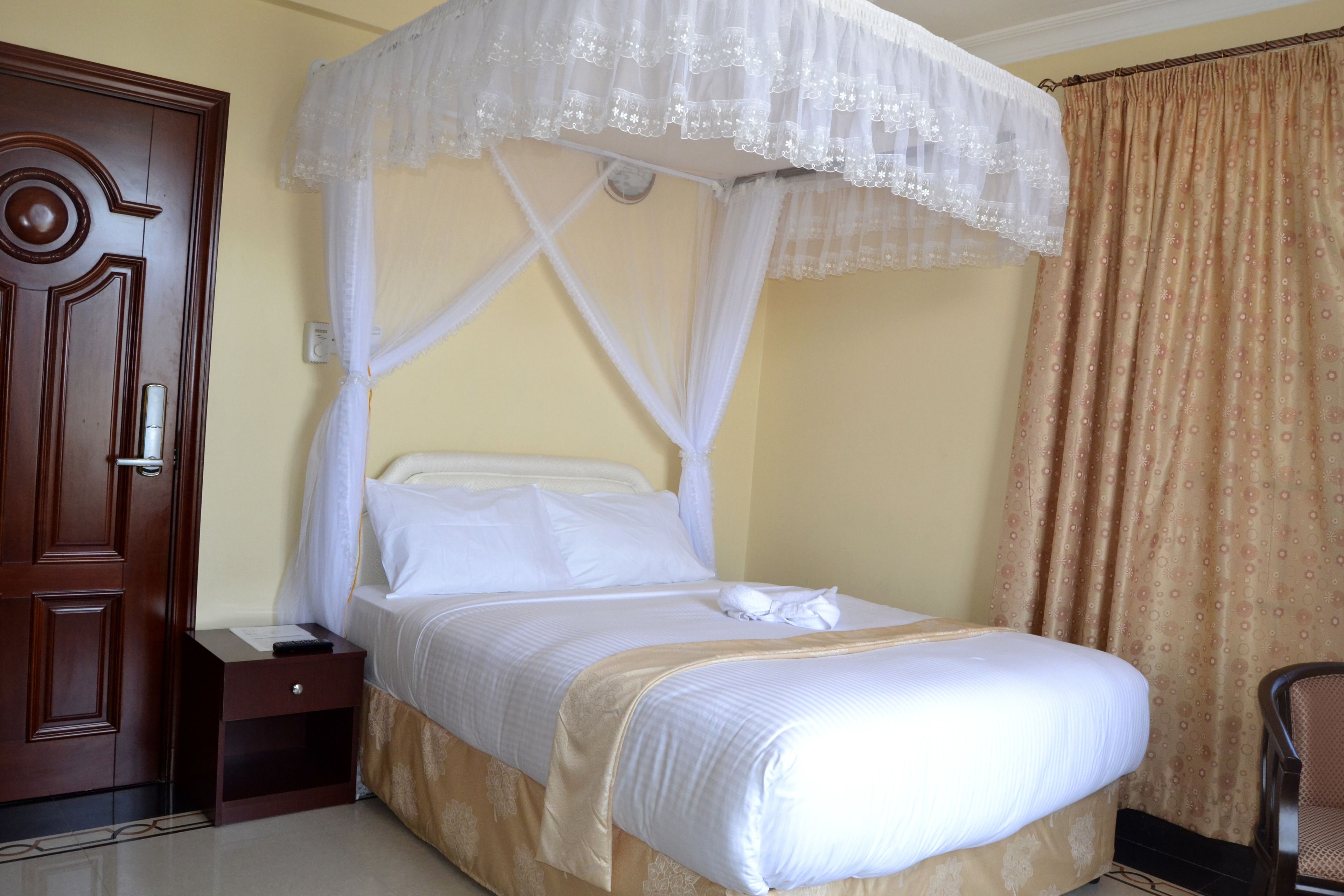 Uma cama bem arrumada com dossel, um criado-mudo de madeira e uma porta marrom.