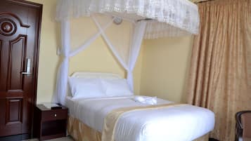 Uma cama bem arrumada com dossel, um criado-mudo de madeira e uma porta marrom.