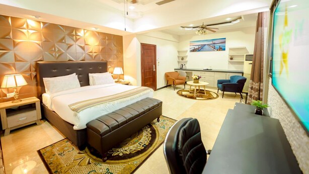 A modern hotel room with a large bed, a desk, a chair, and a dining area.