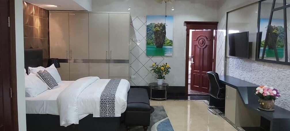 A hotel room with a bed, a desk, a chair, a TV, and a door.