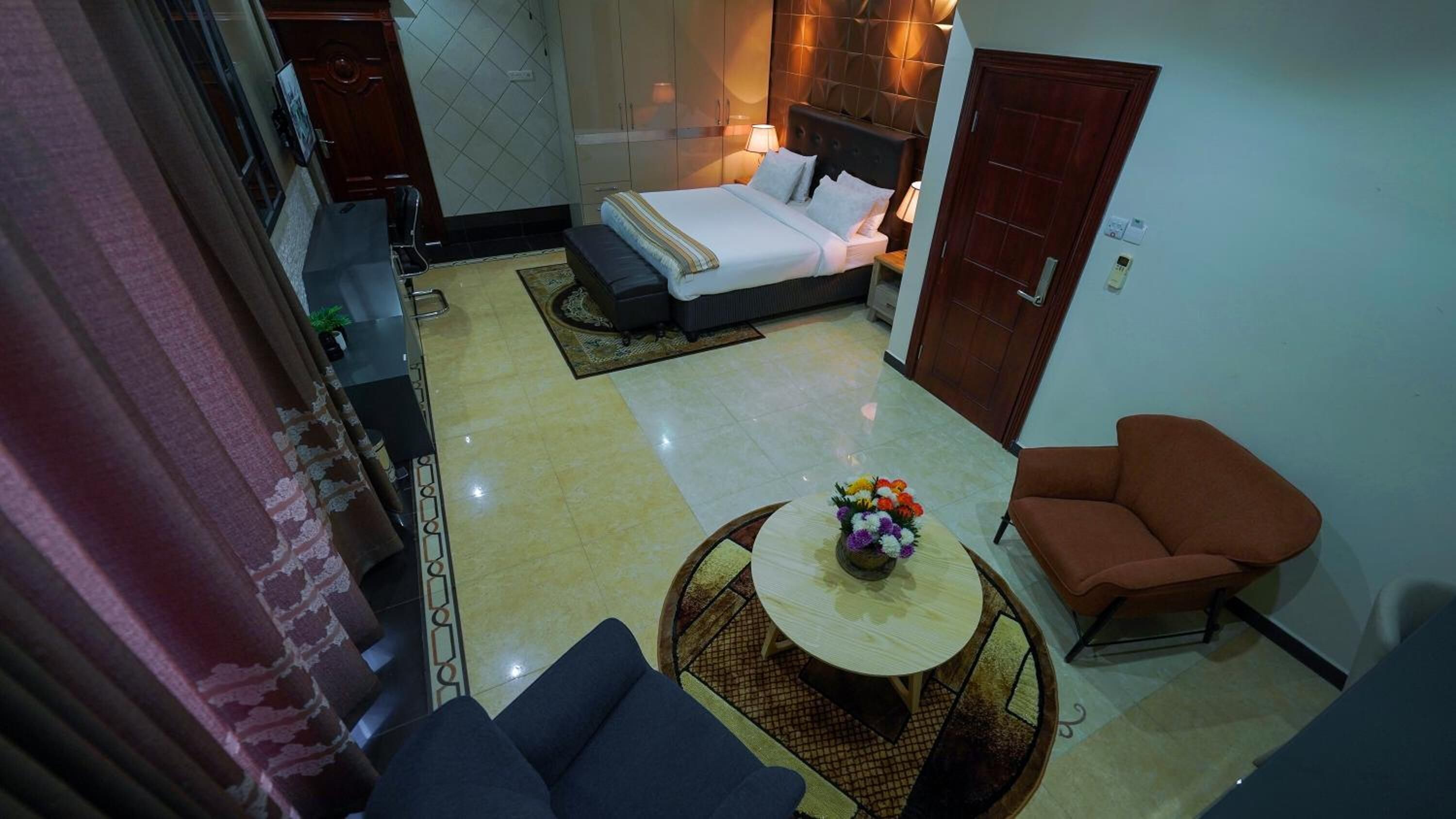 A hotel room with a bed, a small round table with flowers, a sofa, and a chair.