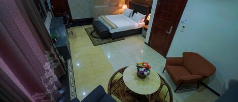 A hotel room with a bed, a small round table with flowers, a sofa, and a chair.