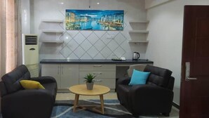 A modern living room with two black sofas, a small round coffee table, and a painting of a cityscape on the wall.