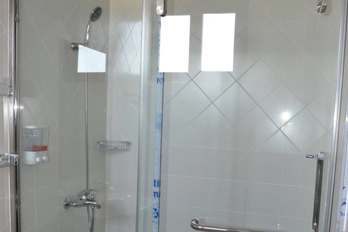 Un box de ducha con paredes de vidrio, una barra de apoyo, un cabezal de ducha y un estante pequeño.