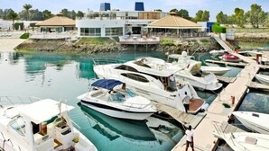 A marina with multiple boats docked, a modern building with a covered area, and a clear view of the water. - C Hotel (Manama)