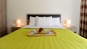 A hotel room with a bed, two bedside lamps, a tray with fruits and cups, and a yellow bedspread. - Rodon Loutra (Kassandra)