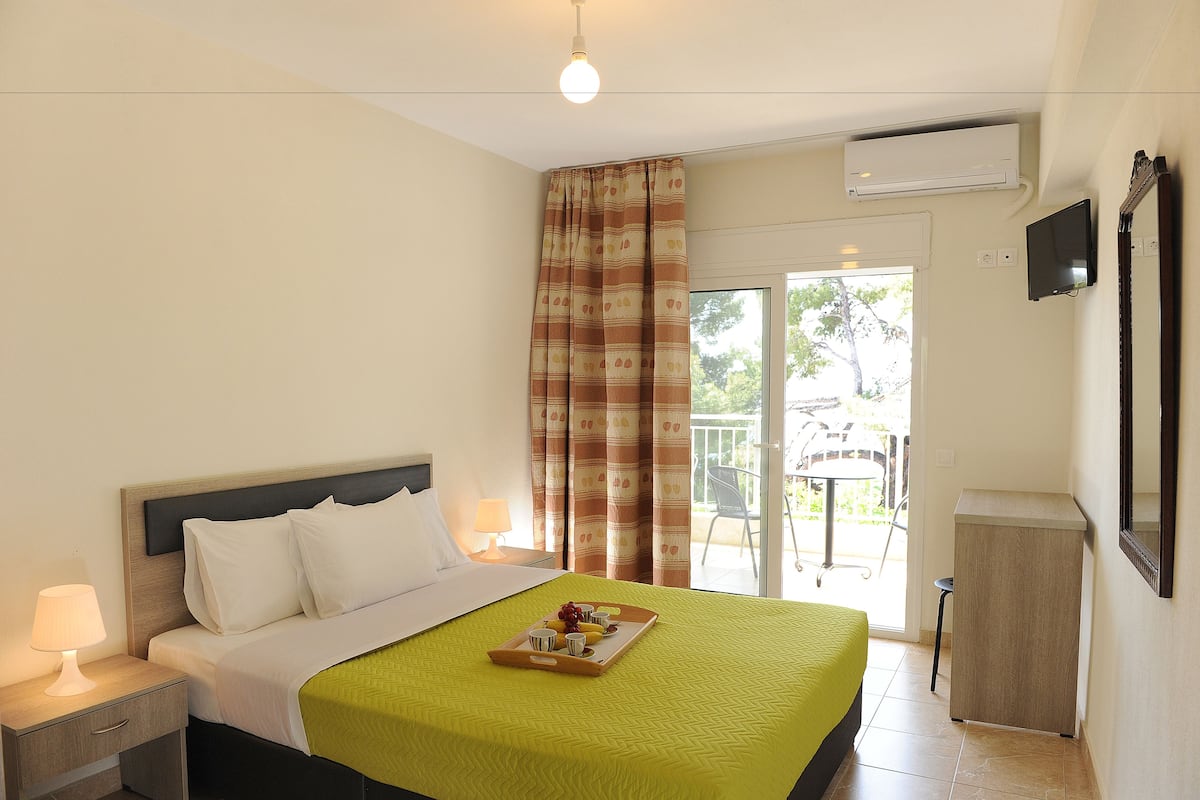 A hotel room with a bed, a bedside table with a lamp, a tray with breakfast items, a TV, and a sliding door to an outdoor area.