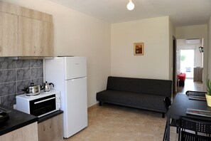 A compact kitchen with a built-in oven, a refrigerator, and a microwave. There is a dark-colored sofa and a dining table with chairs. - Rodon Loutra (Kassandra)