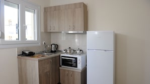 A compact kitchen with wooden cabinets, a built-in oven, a white refrigerator, and a window with a view of buildings outside. - Rodon Loutra (Kassandra)