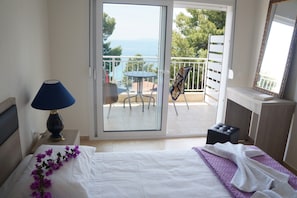 A bedroom with a bed, a nightstand with a lamp, a balcony with a table and chairs, and a view of the sea. - Rodon Loutra (Kassandra)