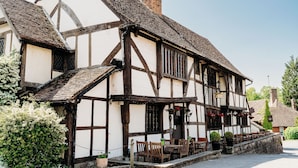 A traditional half-timbered building with a stone staircase leading to a wooden door, surrounded by outdoor seating and potted plants. - The Crown Inn (Godalming)