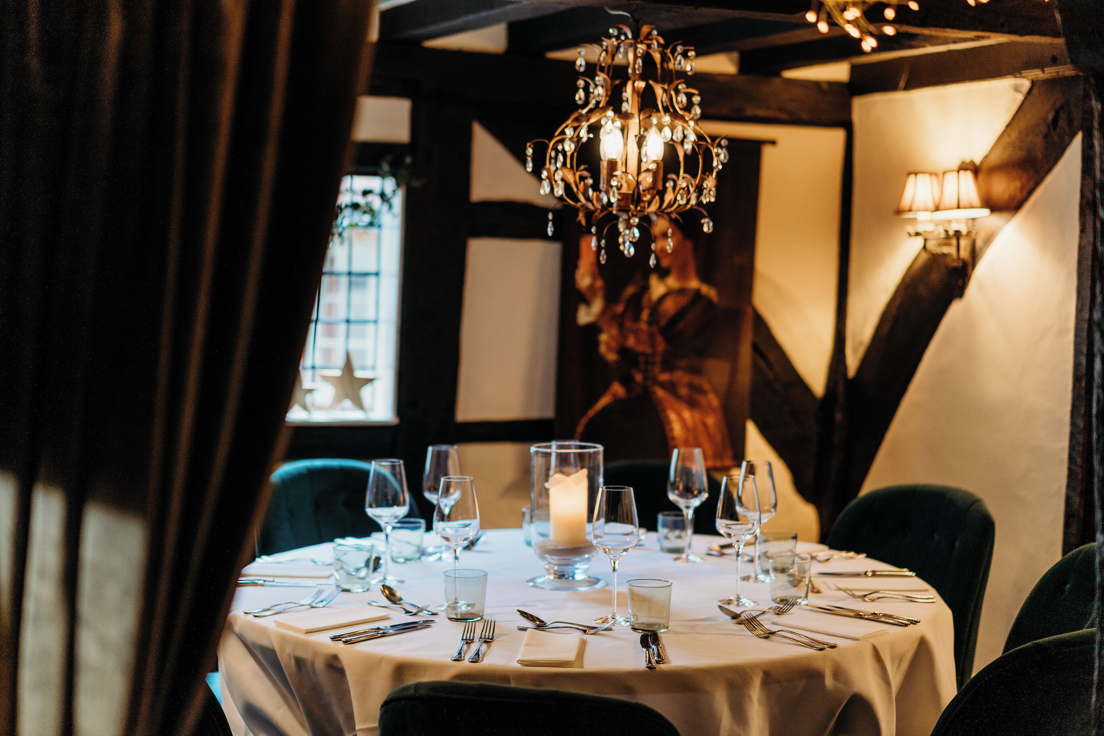 Une table à manger dressée avec de la vaisselle et des couverts, un centre de table composé de bougies et un lustre.