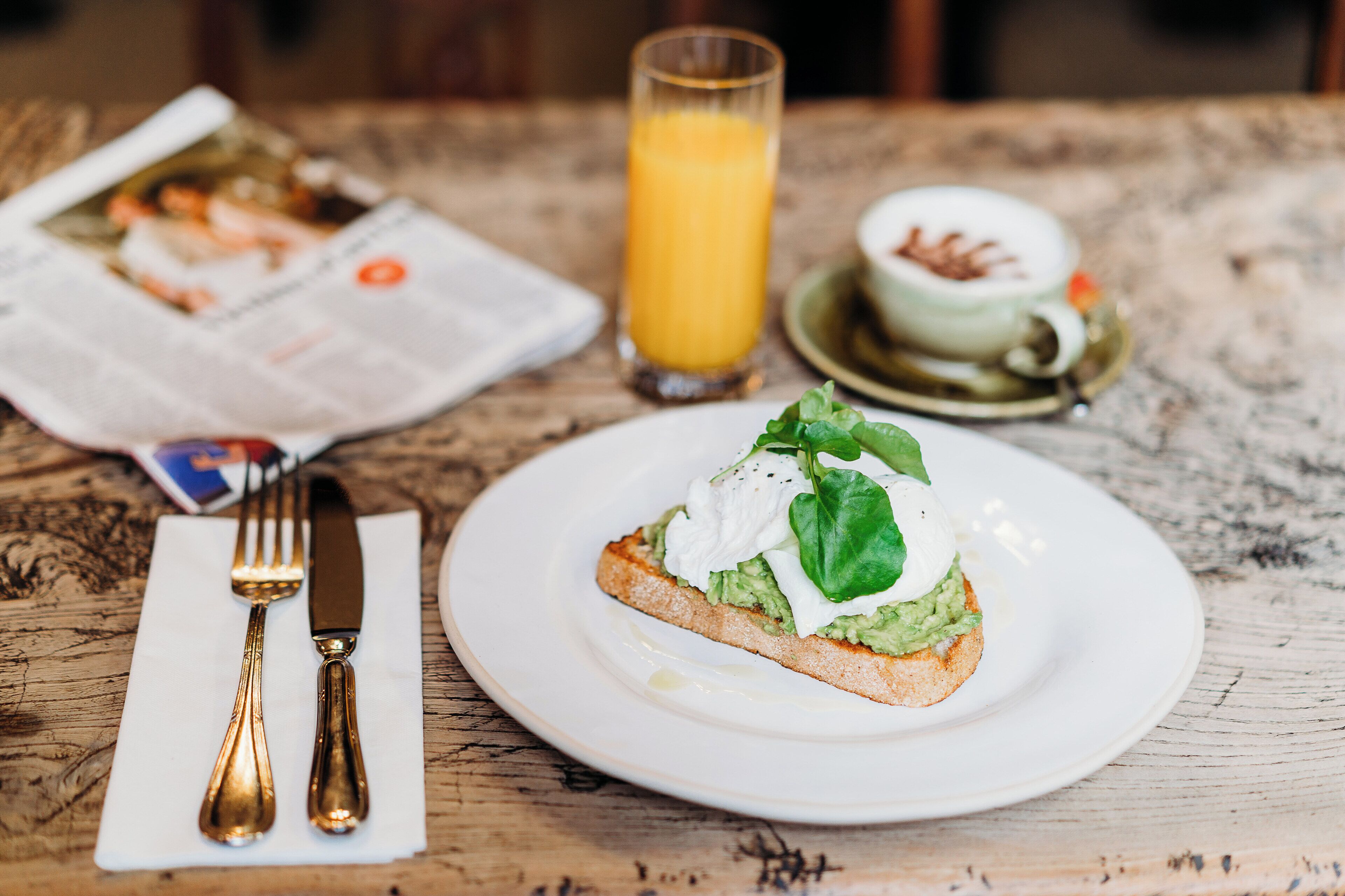 Ein Frühstückstisch mit Avocado-Toast, einem Glas Orangensaft und einer Tasse Kaffee.