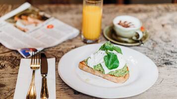 Ein Frühstückstisch mit Avocado-Toast, einem Glas Orangensaft und einer Tasse Kaffee.