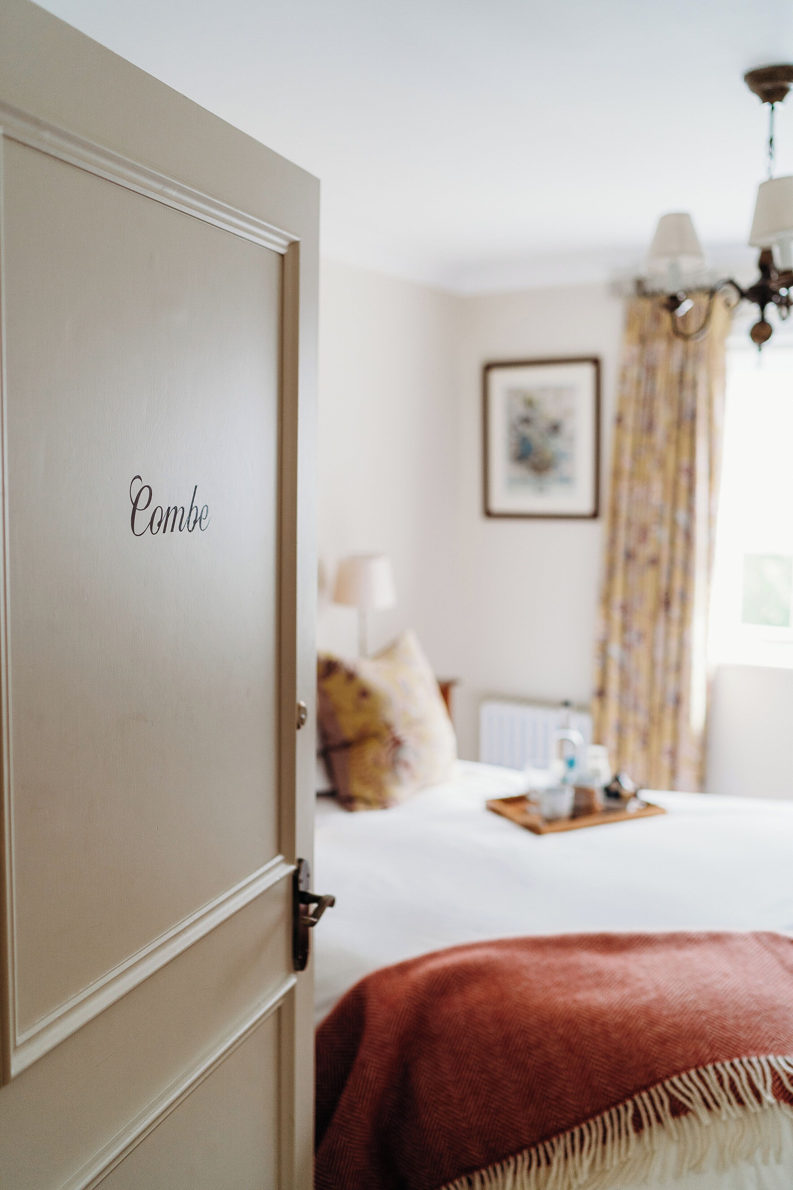 Una habitación con una cama, una puerta con el rótulo "Combe" y un candelabro.