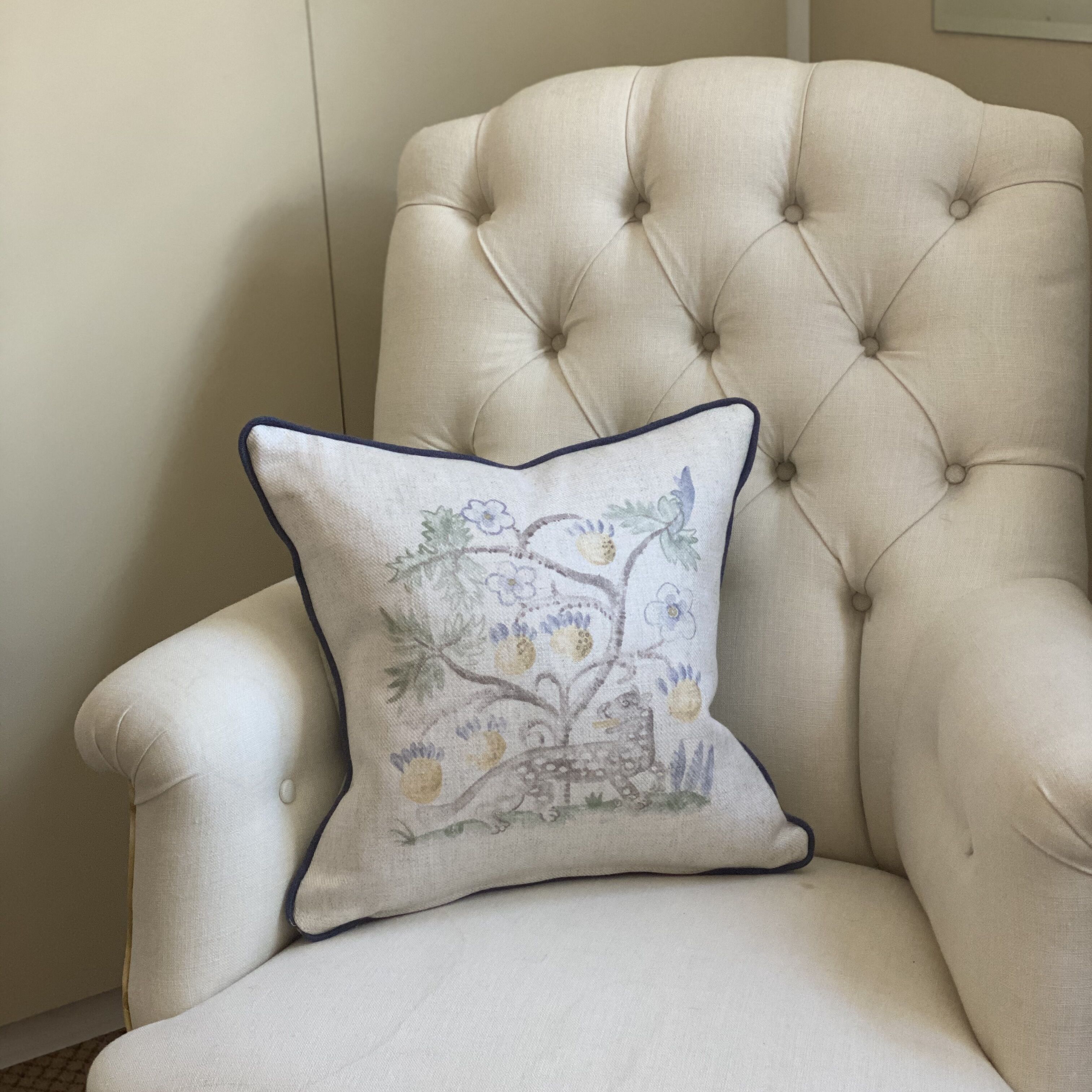 A tufted armchair with a square pillow featuring a floral design.