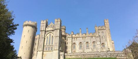 A large, historic castle with multiple towers and arched windows, situated on a grassy hill.