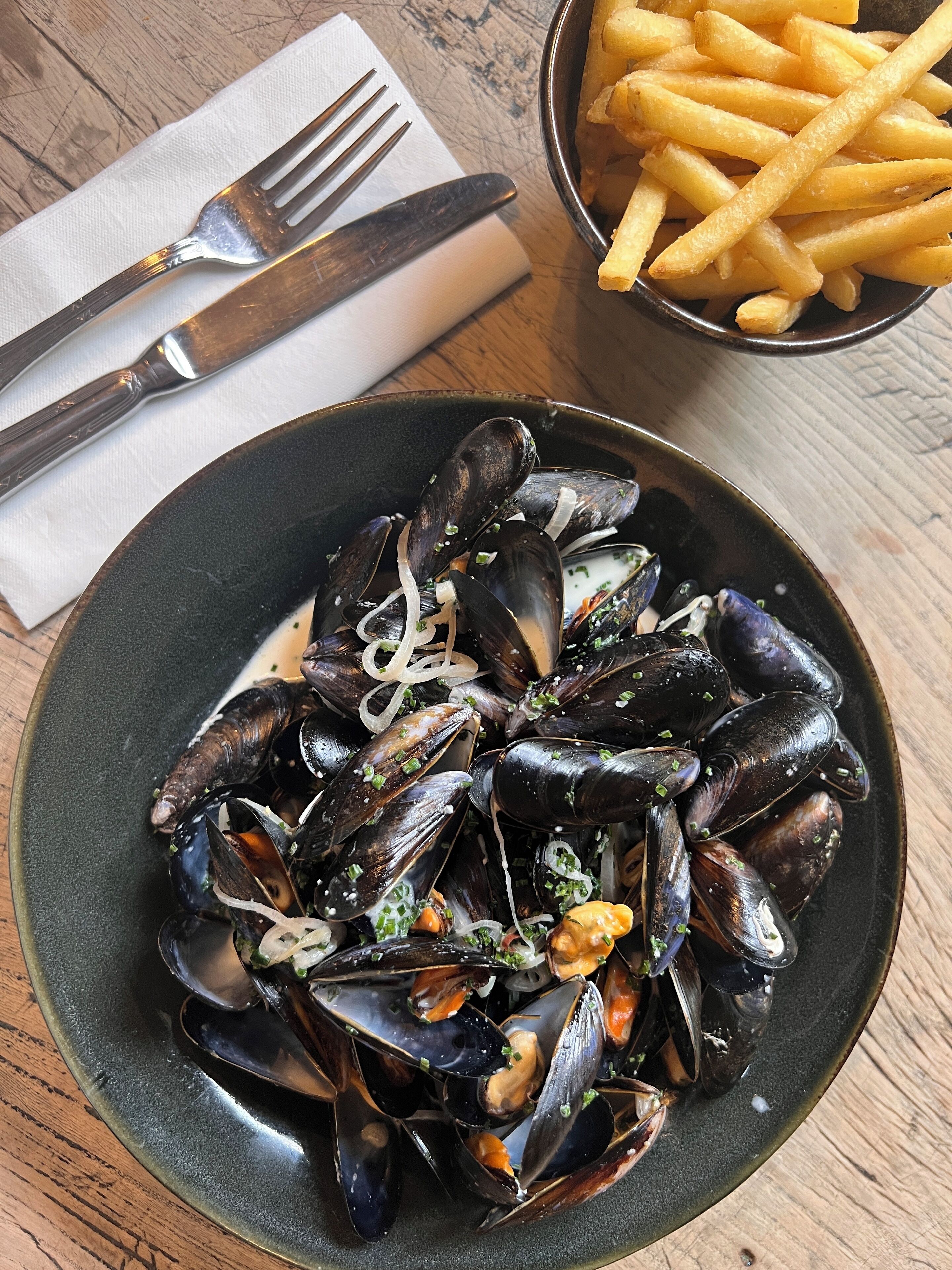 A plate of mussels with a side of fries on a wooden table.