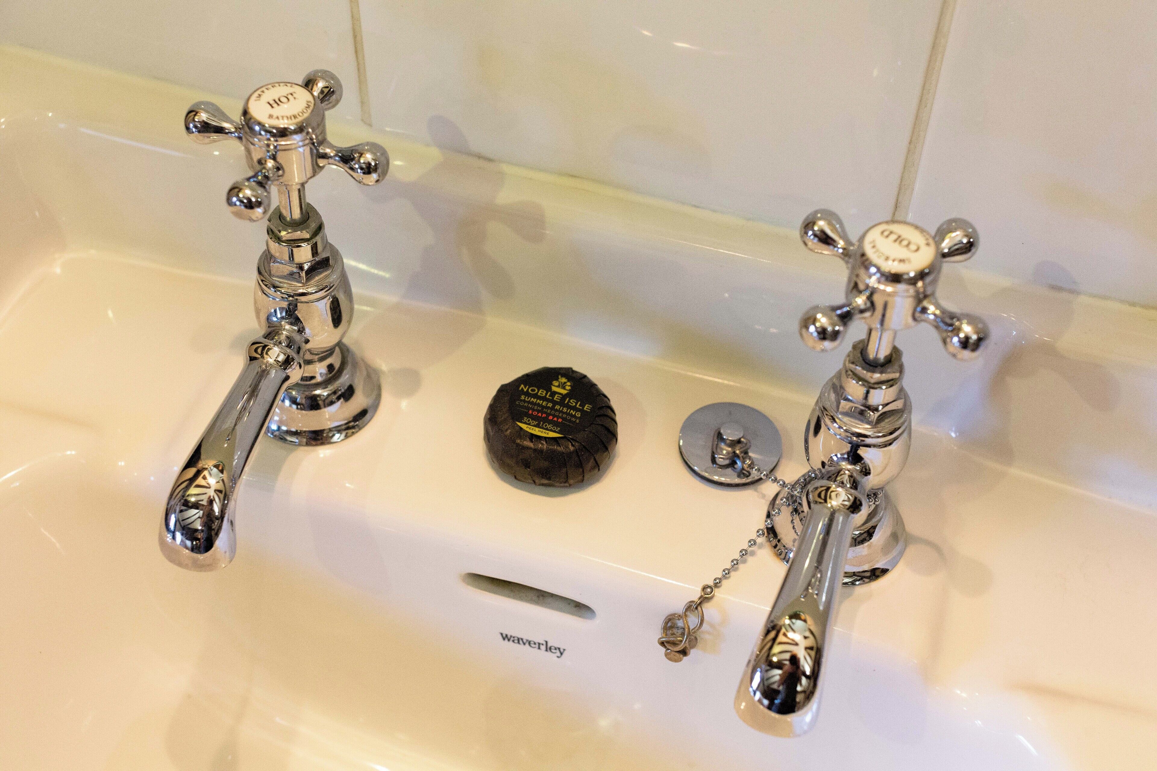 A bathroom with two chrome faucets, a round soap dish, and a small metal object on the sink.