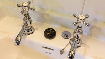 A bathroom with two chrome faucets, a round soap dish, and a small metal object on the sink.