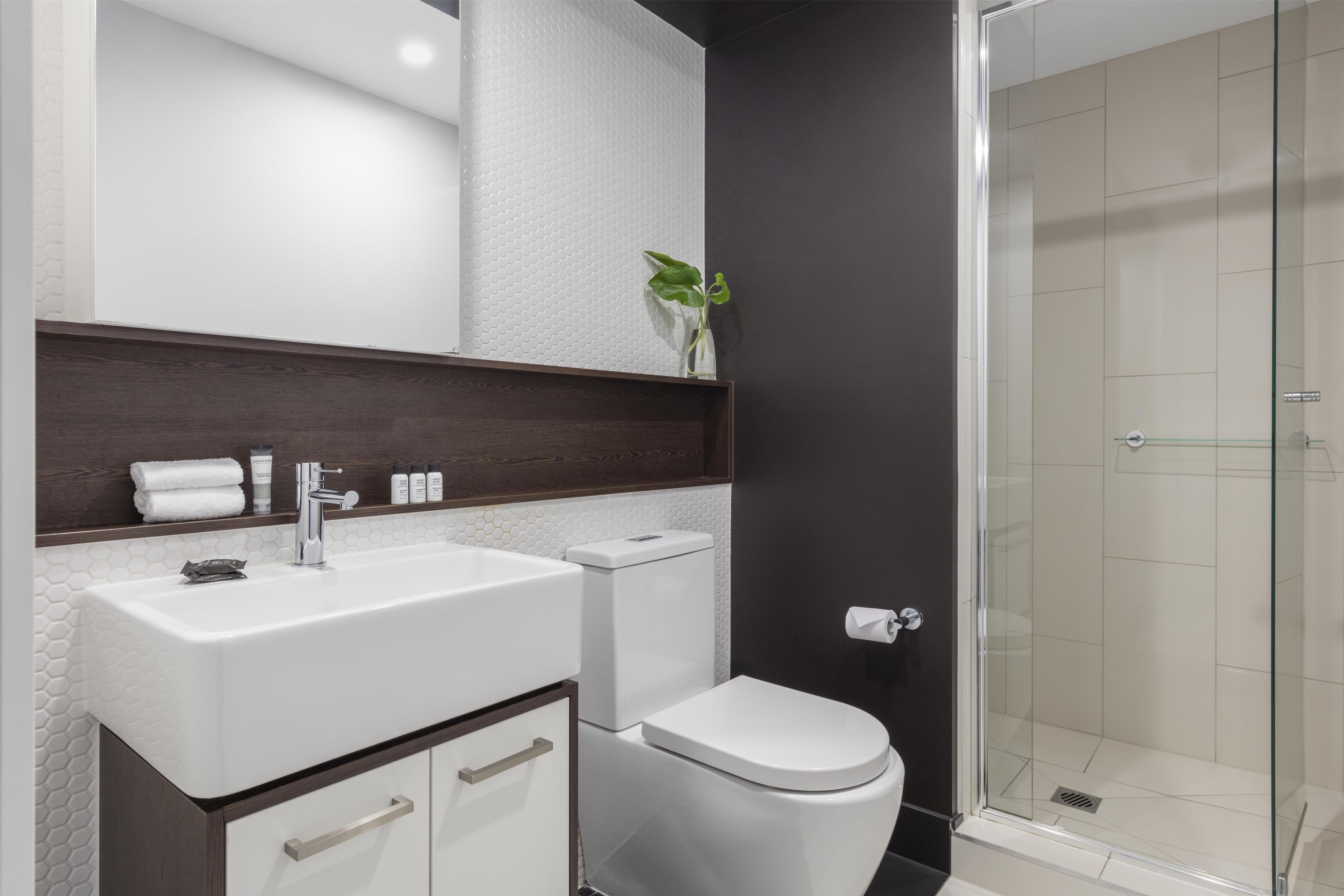 Een moderne badkamer met een wit wastafel, donker houten wastafelmeubel, een toilet en een douchecabine met glazen wanden.
