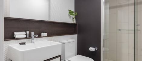 A modern bathroom with a white sink, dark wood vanity, a toilet, and a glass shower enclosure.