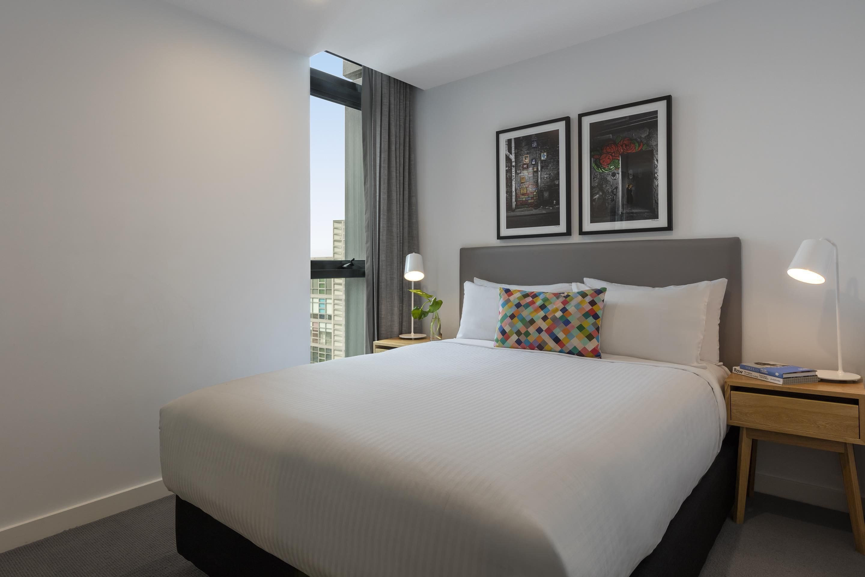 Une chambre d’hôtel avec un grand lit, deux tables de chevet, une fenêtre avec des rideaux et deux tableaux encadrés au mur.