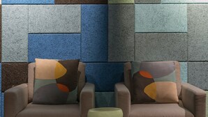 Deux fauteuils ornés de coussins aux couleurs vives, une petite table ronde et un mur à motifs géométriques et à la texture intéressante.