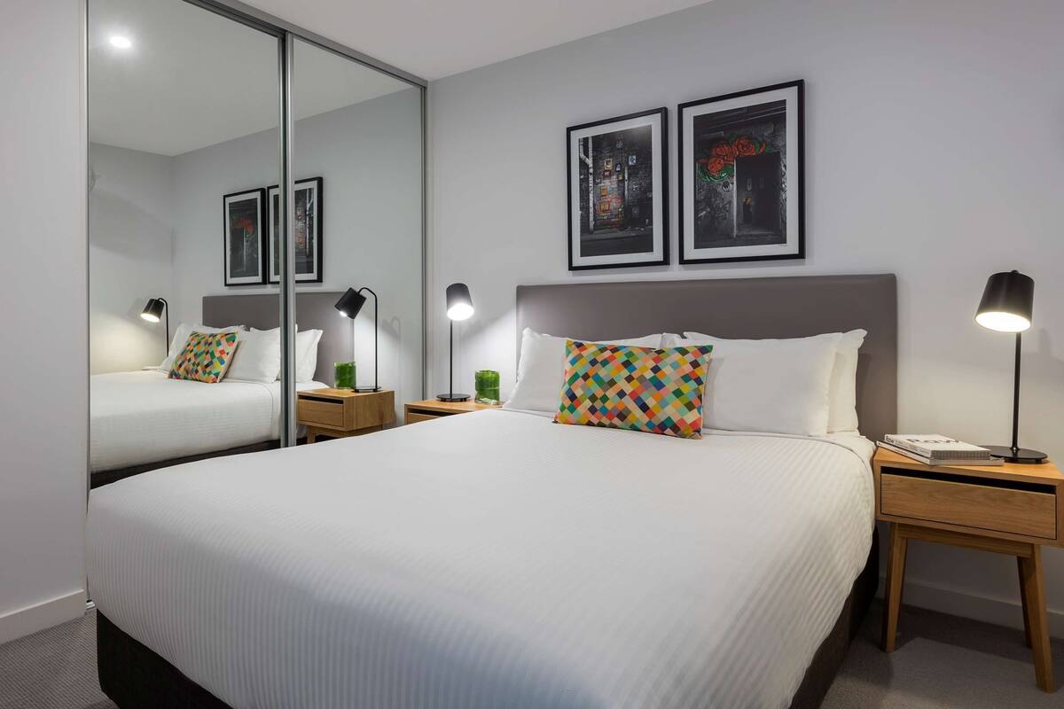 Un cuarto de hotel con una cama grande, dos mesitas de noche, un espejo y cuadros en la pared.