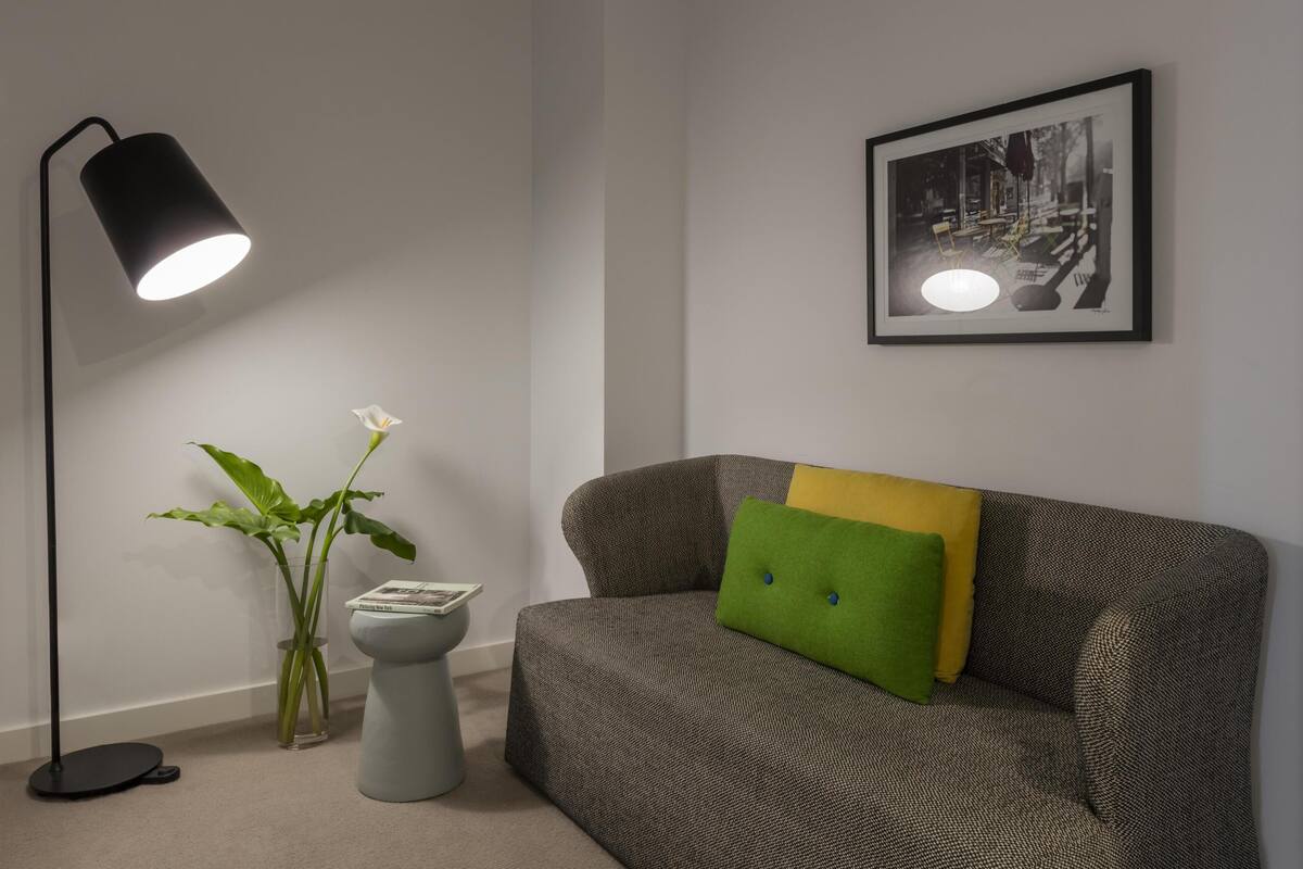 Una habitación con sofá, lámpara de pie, un cuadro en la pared y una planta en maceta.
